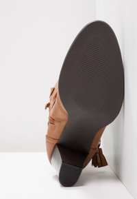 Brauner Lederschuh mit abgerundeter Zehenform, hohen Absatz und einer strukturierten schwarzen Sohle; mit Quastenakzenten und Steppdetails. Größe 37.