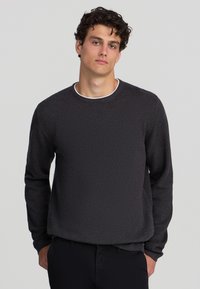 Maglione a maglia grigio scuro con scollatura rotonda, maniche lunghe e un motivo testurizzato. Il materiale sembra morbido con una vestibilità comoda.
