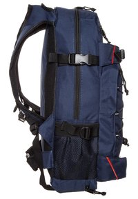 Mochila azul marino con un diseño estructurado, que cuenta con cremalleras, correas ajustables, un bolsillo de malla lateral y detalles de acento en rojo.