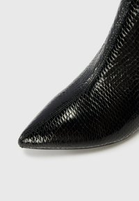 Svart spiss tå-sko laget av blank, teksturert slangeskinnmateriale, med et elegant og strømlinjeformet design.
