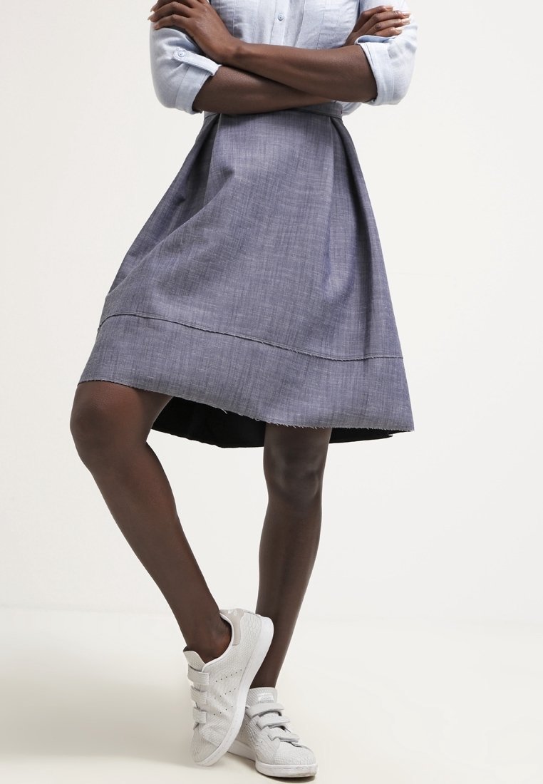 Una falda de chambray gris con forma acampanada, que presenta un dobladillo deshilachado y forro negro; combinada con zapatillas blancas.