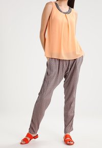 Persikofärgad ärmlös topp med mönstrad halsringning, tillsammans med lösa bruna mönstrade byxor och orange platta sandaler.