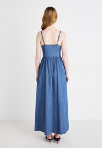 Denim maxikjole med tynne justerbare stropper, tett bodice og samlet liv. Stoffet har en middels blå vask med en jevn tekstur.