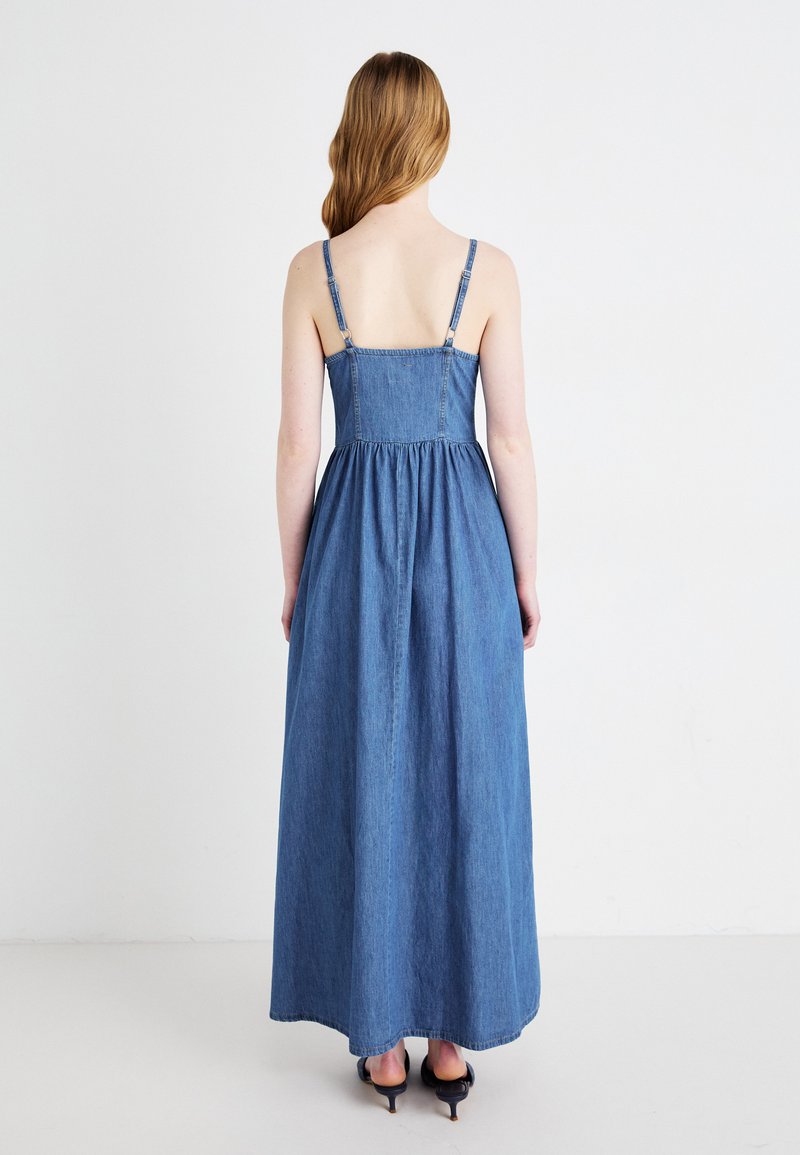 Robe maxi en denim avec de fines bretelles ajustables, un buste cintré et une taille froncée. Le tissu est d'un bleu moyen avec une texture lisse.