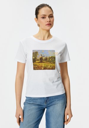 Camiseta blanca de algodón con un estampado de paisaje colorido que presenta un molino de viento, enmarcado por árboles verdes y un cielo amarillo, acentuado por la palabra "Artista."