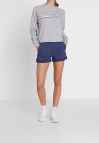 Sudadera gris con un diseño de ola arcoíris, combinada con pantalones cortos azul marino. Zapatillas deportivas blancas completan el atuendo. Estilo simple y casual.