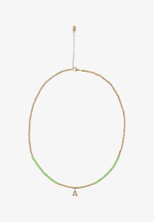 Złoty naszyjnik z koralikami i zielonymi koralikami na froncie, z małą złotą zawieszką w kształcie stylizowanej litery "V" na środku.