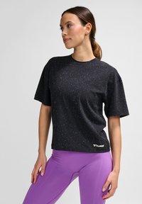 Svart kortärmad T-shirt med prickmönster och rund halsringning. Har en logotyp vid nederkanten. Matchas med lila tajta leggings.