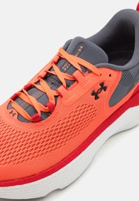 Chaussure de sport orange et grise avec tige en maille, lacets proéminents, semelle intercalaire en mousse et semelle extérieure en caoutchouc. Comprend des détails texturés et un accent de logo.