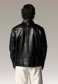 Veste en cuir noire avec un design simple, dotée d'un col montant, d'une couture au dos et d'un détail en étiquette orange. Texture lisse et silhouette ajustée.