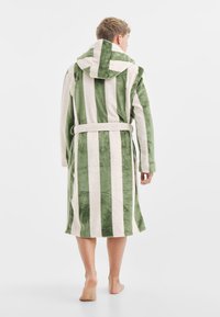Gestreepte badjas in groen en crèmekleur; gemaakt van zacht, pluche materiaal. Bevat een capuchon, lange mouwen en een strikband.