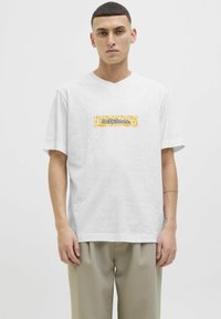 Hvid bomulds t-shirt med v-hals, med et gult og sort "Jack & Jones" logo i et rektangulært design på forsiden.