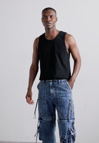 Un maiou negru cu dungi, asociat cu blugi cargo de un albastru deschis, multi-buzunare, cu fermoare și o sfoară ajustabilă la manșete.