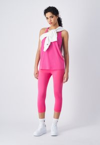 Top rosa sin mangas y leggins capri con zapatillas blancas. Sudadera blanca atada en los hombros. Tejido suave, diseño ajustado.