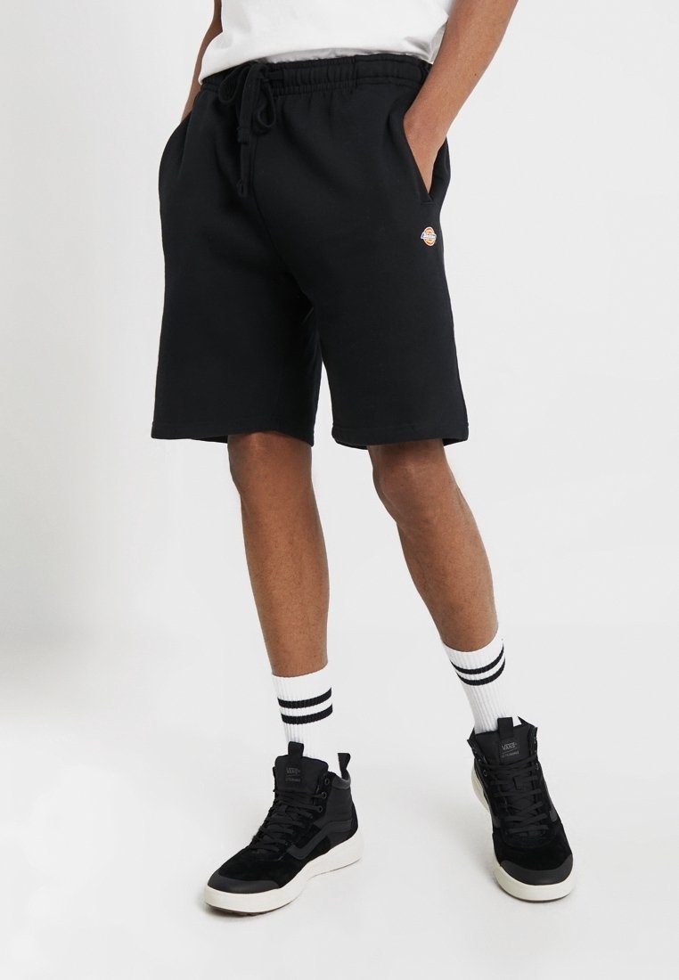 Černé bavlněné šortky s elastickým pasem, bočními kapsami a malou nášivkou s logem. V kombinaci s černými vysokými teniskami a pruhovanými ponožkami.