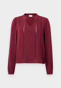 Blouse bordeaux à manches longues avec un col en V, en tissu texturé, plis avant et poignets élastiques. Couture détaillée le long des côtés.