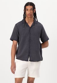 Chemise à manches courtes pour hommes en tissu gris foncé avec un motif texturé, assortie à un short beige clair.