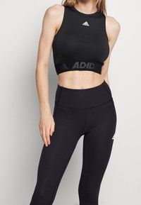 Top corto deportivo negro con escote redondo y logotipo, combinado con leggins negros de cintura alta con diseño sin costuras y una sutil marca.
