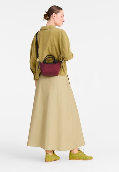 Small burgundy handbag with black handles, paired with a light green suede jacket and a beige maxi skirt. Green sneakers complete the outfit.
