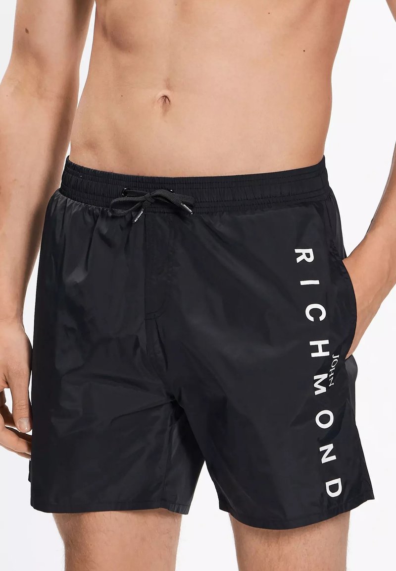Pantaloni da bagno neri realizzati in tessuto leggero, con vita elastica, coulisse e una grande scritta bianca "RICHMOND" sul lato.