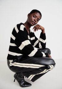 Zwart-wit gestreepte gebreide trui, zwarte leren broek met witte zijstrepen, en zwart leren laarzen met hoge hakken en zilveren studs.