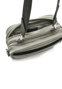 Graue kompakte Tasche mit mehreren Reißverschlussfächern, glatter Oberfläche und abnehmbarem Schultergurt. Verfügt über metallische Hardware-Elemente.