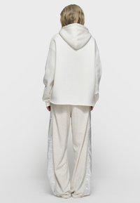 Sudadera con capucha blanca de corte holgado y una capucha grande, combinada con pantalones deportivos de pierna ancha en gris claro, con franjas laterales plateadas brillantes.