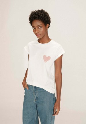 T-shirt blanc à manches courtes avec un motif de cœur rose clair sur la poitrine gauche. Associé à un jean bleu. Texture de tissu naturel.