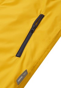 Veste imperméable jaune avec une fermeture éclair bleu marine et une petite étiquette en tissu portant la mention "reima TEC". Texture lisse avec un léger éclat.