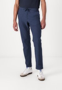Blue, lightweight trousers with an elastic waistband, drawstring, side pockets, and a straight cut. Worn with white and grey sneakers.