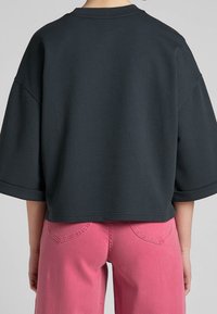 Sudadera negra de gran tamaño con mangas cortas, tejido texturizado y cuello de canalé, combinada con pantalones de pierna ancha rosas que tienen bolsillos traseros.