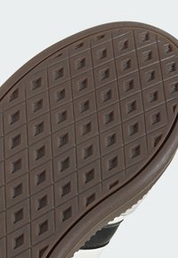 Brown rubber shoe sole with a textured, square pattern, featuring diamond-shaped accents and rounded edges. Smooth side for support.