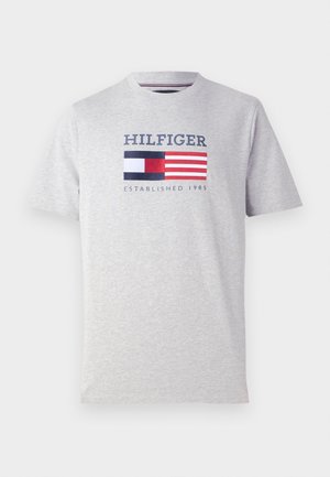 T-shirt gris clair à manches courtes avec le texte "HILFIGER", graphique du drapeau rouge, blanc et bleu, et "ESTABLISHED 1985" imprimé sur le devant.