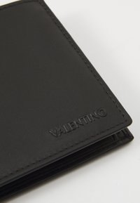 Crna kožna novčanica s utisnutim logom "VALENTINO", s čistim šavovima i savijenim dizajnom. Glatka tekstura, minimalistički izgled.