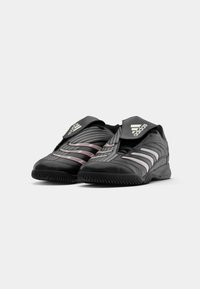 Scarpe atletiche nere con strisce grigie e rosse, caratterizzate da un design slip-on e un colletto imbottito. Suola in gomma con motivo di presa testurizzato.