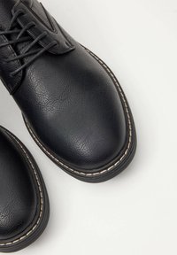 Zapatos de cuero negro con acabado texturizado, puntera redondeada y detalles de costura en contraste. Diseño con cordones y suelas de goma duraderas.