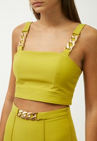 Top recortado en verde lima con tirantes anchos que presenta acentos de cadena dorada. Tela suave, diseño ajustado y detalles de costura en el dobladillo.