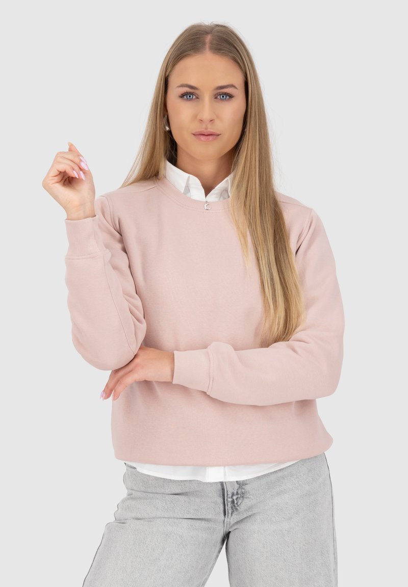 Maglione rosa chiaro realizzato in tessuto morbido, con scollatura girocollo e polsini a costine, abbinato a una camicia bianca con colletto sotto.
