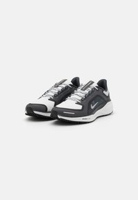 Schwarz-weiße Nike-Laufschuhe mit Netzpaneelen, kontrastierenden Schnürsenkeln und strukturiertem Gummisohle. Mit einem auffälligen Logo an der Seite.