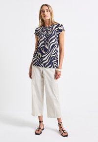 Top corto a maniche corte navy e crema con stampa a zebra ondulata e scollatura plissettata. Abbinato a pantaloni larghi di colore chiaro e sandali neri con cinturini.