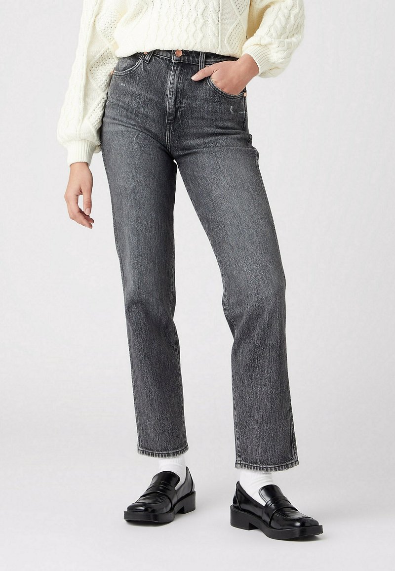Jeans de tiro alto y pierna recta en denim gris oscuro, con cinco bolsillos y cierre de botón. Combinados con un suéter de punto crema y mocasines negros.