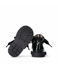 Stivali alla caviglia in pelle verniciata nera con suola in gomma spessa e testurizzata e lacci decorativi. Presenta una cinghia con marchio sul retro.