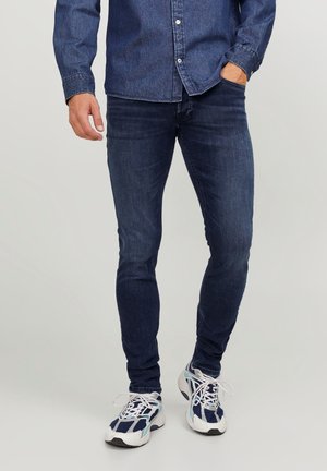 Jean en denim skinny-fit bleu foncé, avec un léger délavage et un design à cinq poches, accompagnés de chaussures de sport en mesh blanches et marines.