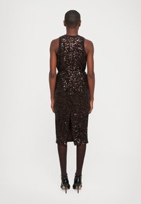 Vestido midi sin mangas de lentejuelas marrón oscuro con abertura en la espalda, combinado con medias oscuras y zapatos de tacón alto de charol negro.