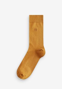 Sok iz gorčične barve, izdelan iz gladkega, mehkega materiala. Ima rebrast rob in majhen embosiran logotip blizu vrha.