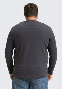 Langarmshirt in donkergrijs met een gladde textuur, gecombineerd met lichtblauwe denim jeans met stiksels op de achterzakken.