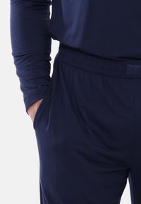 Marineblauw, langärmelig topje gecombineerd met bijpassende broek met een elastische tailleband en zijzakken. Gladde, rekbare stoftextuur.