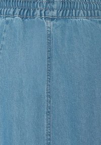 Lichtblauwe denimstof met een gladde textuur, voorzien van een elastische tailleband en verticale naaddetails.