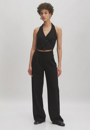 Zwarte halternek crop top met een enkele knoopsluiting, gecombineerd met wijde broekspijpen. Gladde stof met een getailleerde pasvorm en zonder patronen.