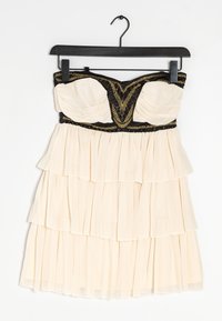 Axelösa klänning med krämfärgad tyg och lager av volanger. Svart överdel prydd med intrikat guldbroderi. Mjuk, flödande textur.